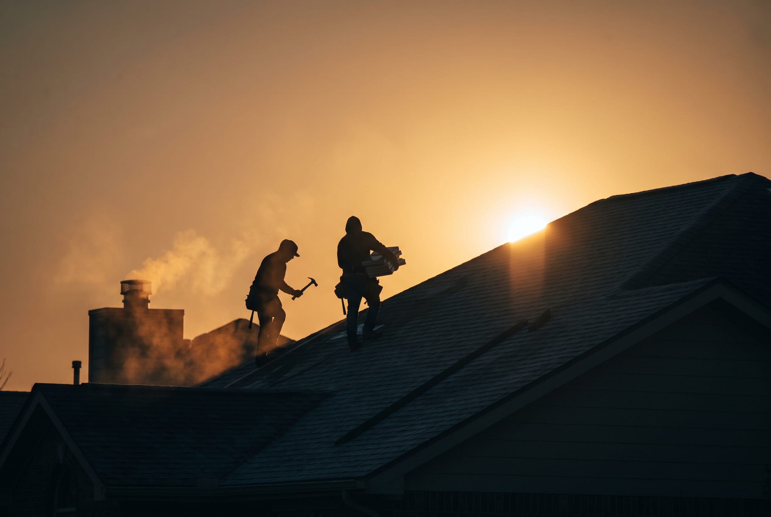 Two roofers at work on a roof at sunrise