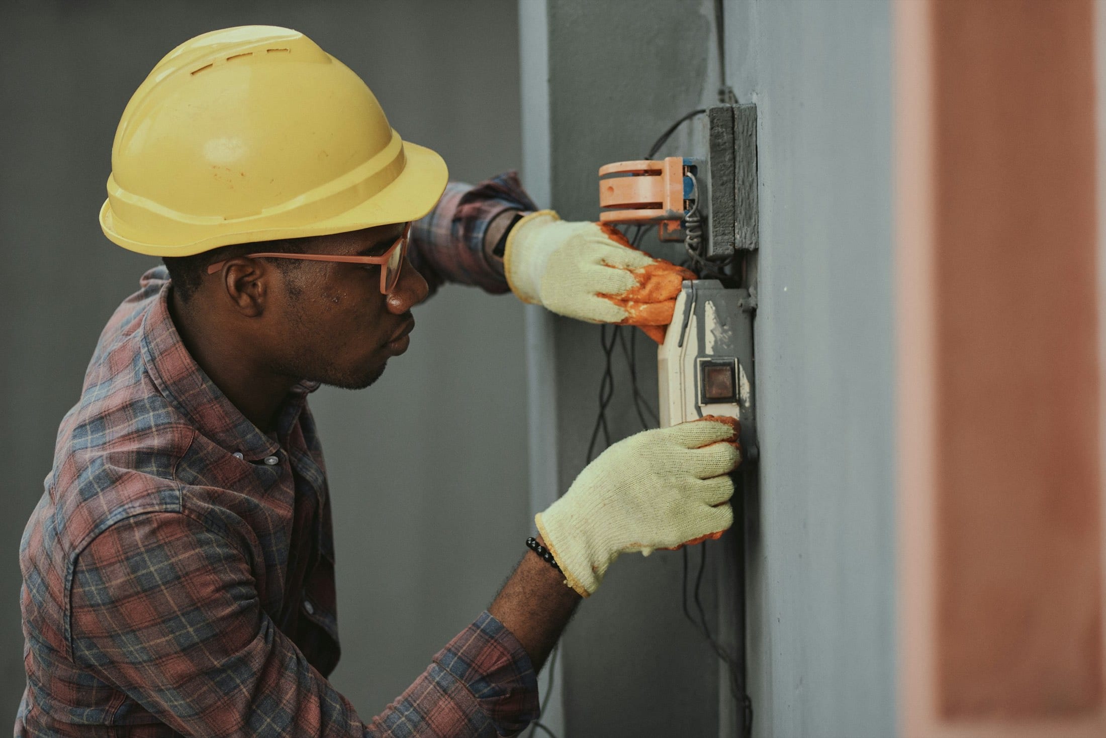 Electrician in a hardhat wiring a junction box on a wall