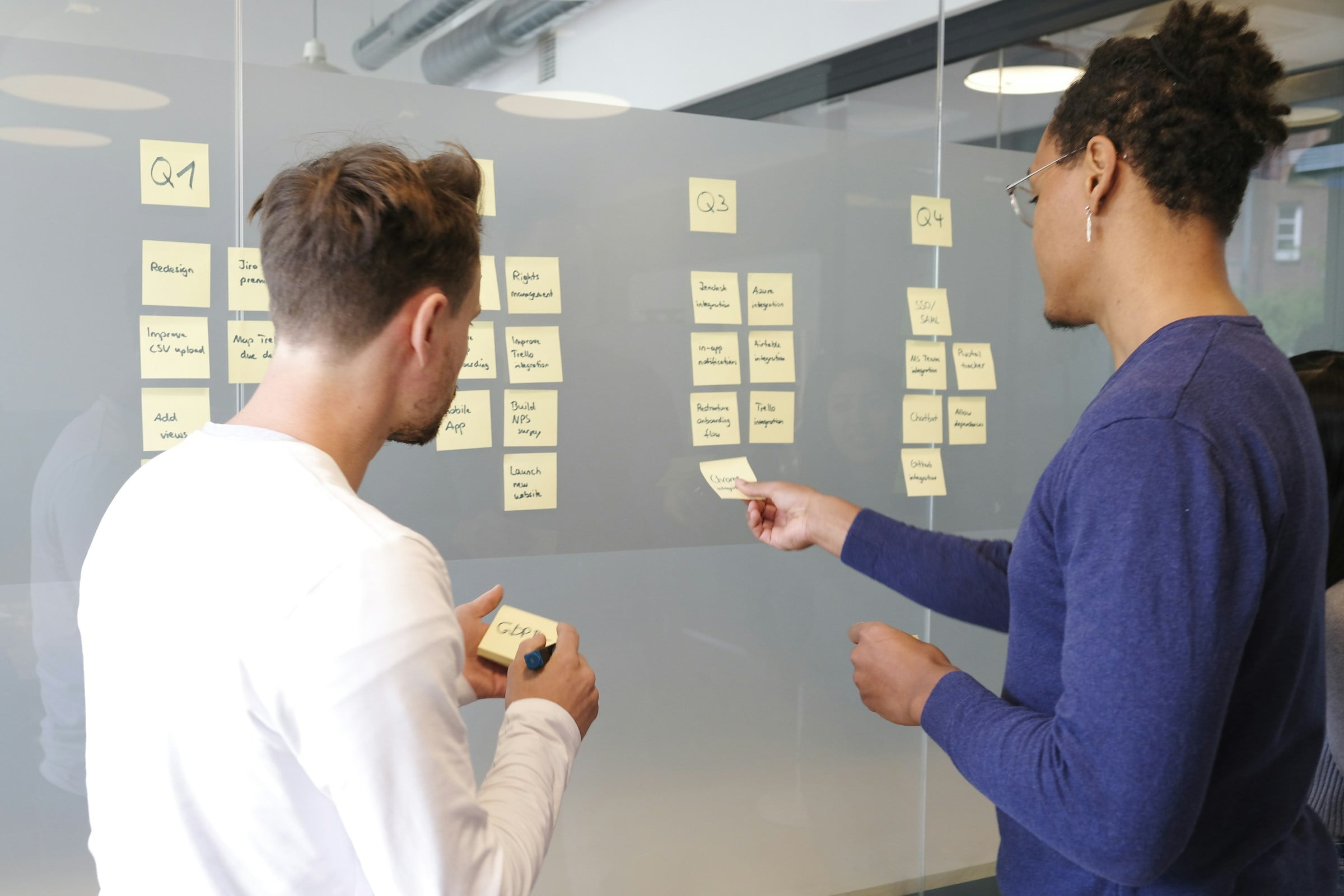 Two people planning a quarterly roadmap with sticky notes on a glass wall