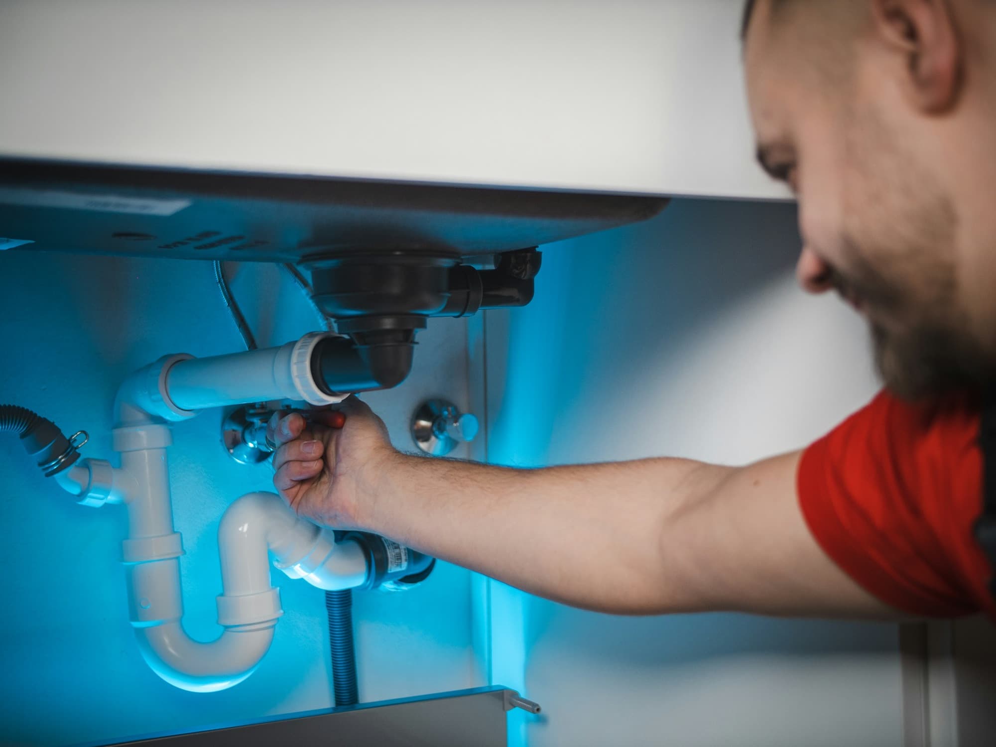 Technician clearing a clogged drain pipe connection under a cabinet