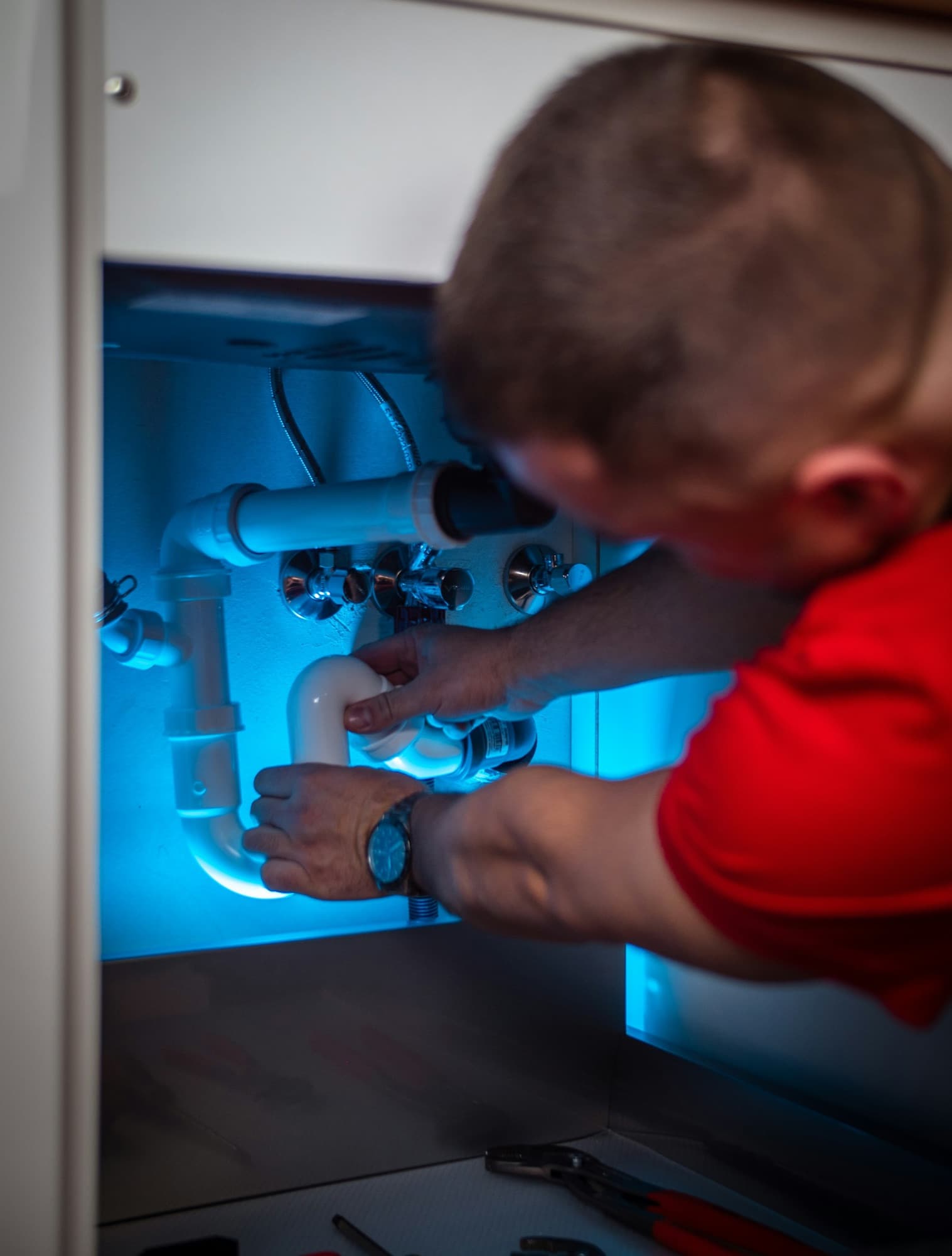 Plumber reaching into a cabinet to service a supply line