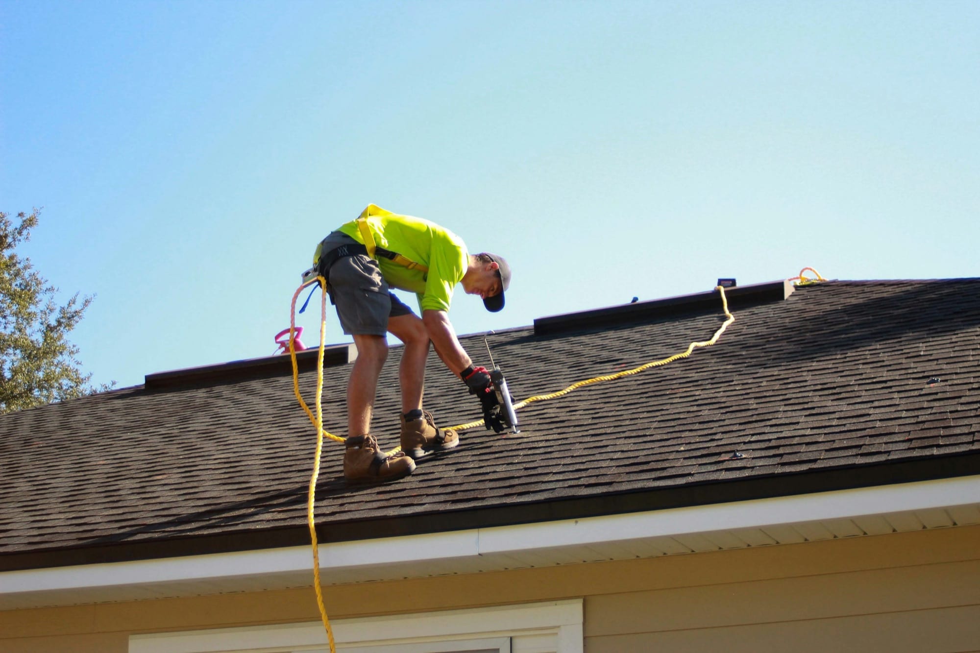 A roofer in a high-visibility shirt installing new architectural shingles on a home