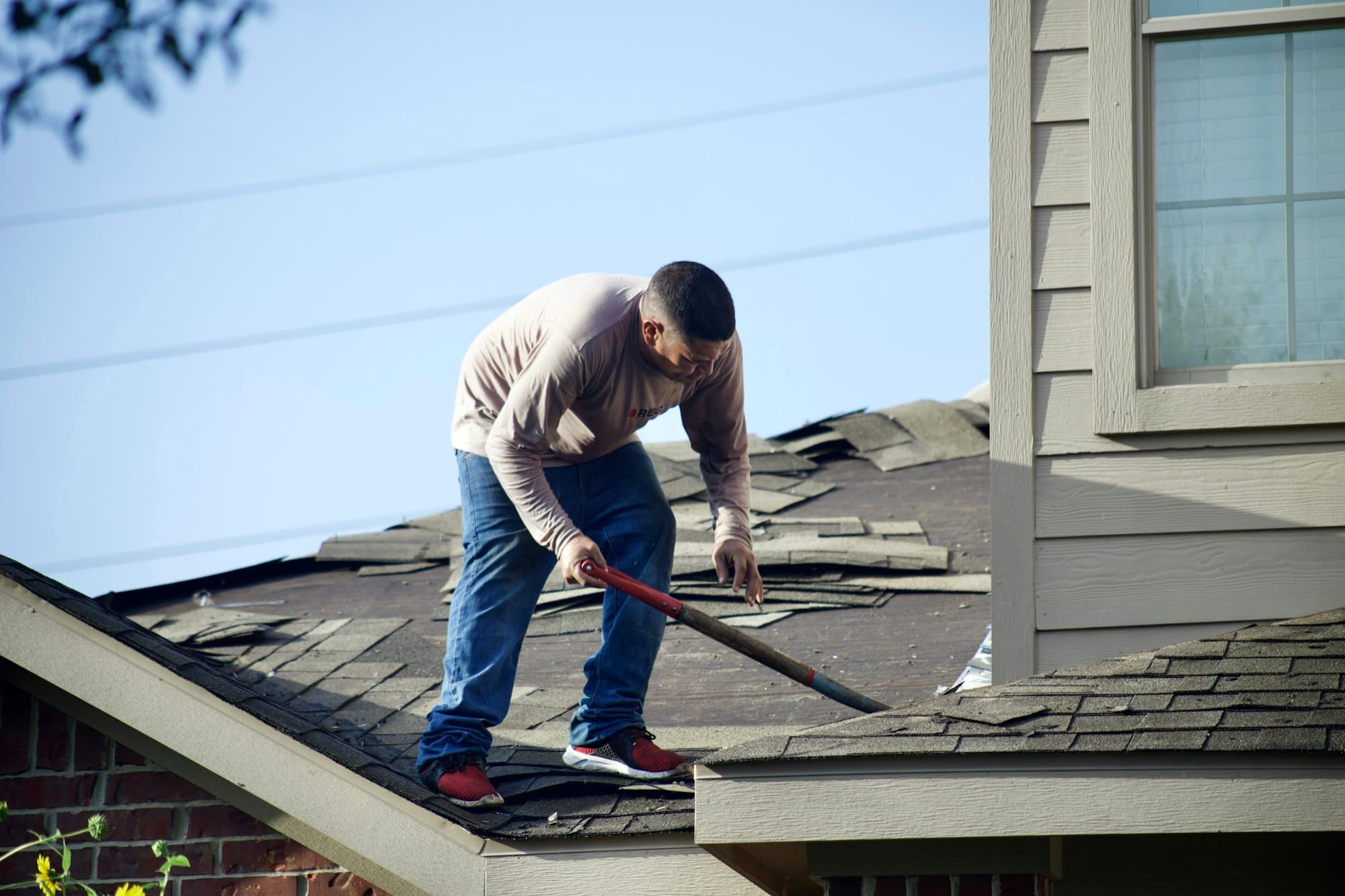 A roofer removing damaged shingles during a tear-off